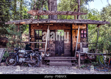 Nis, Serbien - Juli 11, 2018: Großes Modell von Wild West Saloon und altes Motorrad vor dem Haus in der Natur. El Dorado text auf Holzbrett Stockfoto