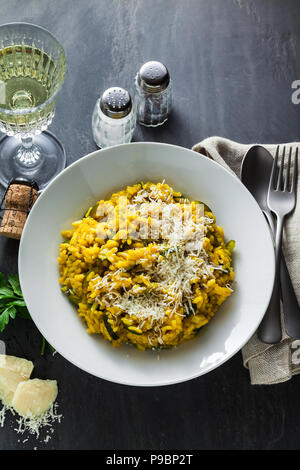 Italienische Gericht gelben risotto milanese mit Safran, Zucchini und Parmesan auf schwarzem Schiefer Tisch mit Weißwein im Glas. Nord Italien Küche Stockfoto