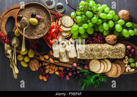 Holz-, das Board mit veganen Snacks. Pastete von Oliven und Käse aus cashewnüsse mit Kräutern. Gesunde Vorspeise mit Trauben, Nüssen, getrockneten Früchten o Stockfoto
