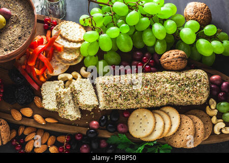 Holz-, das Board mit veganen Snacks. Pastete von Oliven und Käse aus cashewnüsse mit Kräutern. Gesunde Vorspeise mit Trauben, Nüssen, getrockneten Früchten o Stockfoto