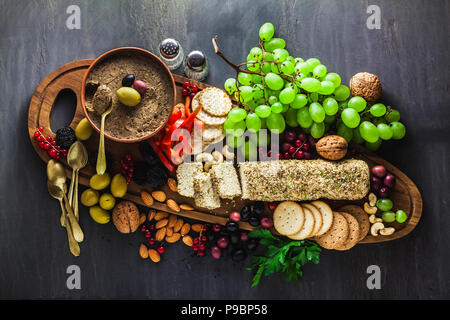 Holz-, das Board mit veganen Snacks. Pastete von Oliven und Käse aus cashewnüsse mit Kräutern. Gesunde Vorspeise mit Trauben, Nüssen, getrockneten Früchten o Stockfoto