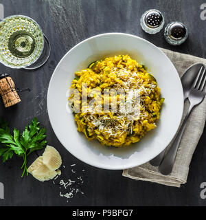 Italienische Gericht gelben risotto milanese mit Safran, Zucchini und Parmesan auf schwarzem Schiefer Tisch mit Weißwein im Glas. Nord Italien Küche Stockfoto