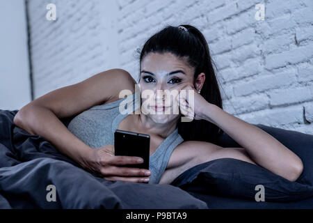 Junge schöne Latin Frau auf dem Bett bis spät in die Nacht reden und über Handy gelangweilt und der Verwendung von Smart Handy im Internet Kommunikation müde Stockfoto