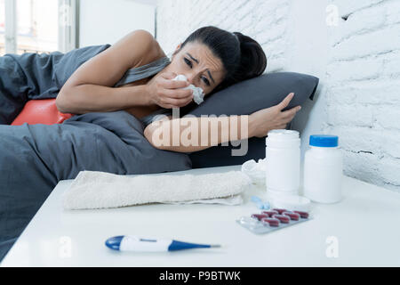 Sick Hispanic Frau im Bett, die kranken Tag weg von der Arbeit thermometer Temperatur für Fieber zu überprüfen und Vitamine Wärmflasche und Gewebe in c Stockfoto