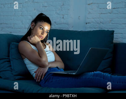 Junge schöne hispanic Internet-süchtiger Frau in legere Kleidung sitzen auf der Couch gebohrt und mit Laptop müde spät in der Nacht in da Stockfoto