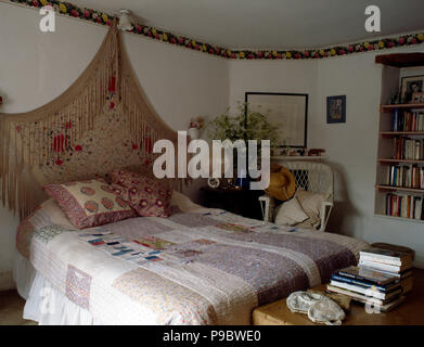 Vintage Schal an der Wand über dem Bett mit einem Patchwork Quilt in einem Ferienhaus Schlafzimmer mit einem geblümten Tapeten Grenze Stockfoto