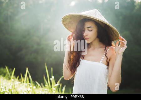 Portrait von jungen asiatischen Frau in traditioneller balinesischer Strohhut. Morgensonne in Ubud Reisfelder. Die chinesische Kultur Stockfoto