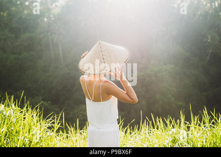 Portrait von jungen asiatischen Frau in traditioneller balinesischer Strohhut. Morgensonne in Ubud Reisfelder. Die chinesische Kultur Stockfoto