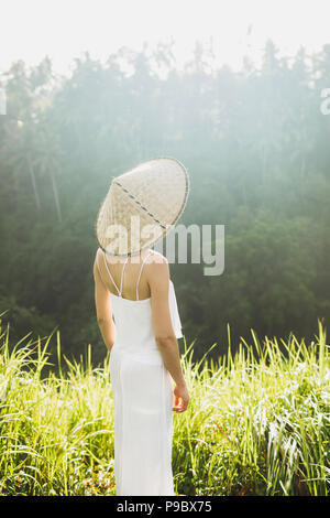 Portrait von jungen asiatischen Frau in traditioneller balinesischer Strohhut. Morgensonne in Ubud Reisfelder. Die chinesische Kultur Stockfoto