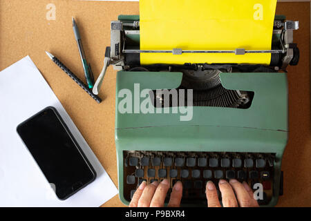 Zwei Mann hand Tippen auf Vintage old Mint Green Thai Schreibmaschine mit einfachen gelbes Papier auf crok Holzbrett mit Stiften und Handy an der Seite. Stockfoto