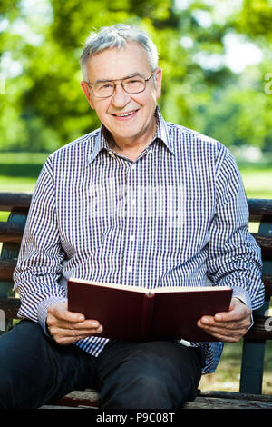 Älterer Mann ein Buch lesen im Park Stockfoto