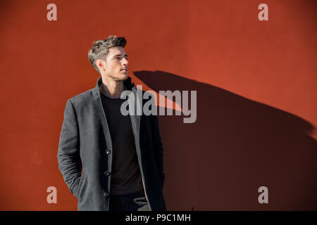 Junger Mann in einem Winter Outfit lehnte sich auf Rote Wand Stockfoto