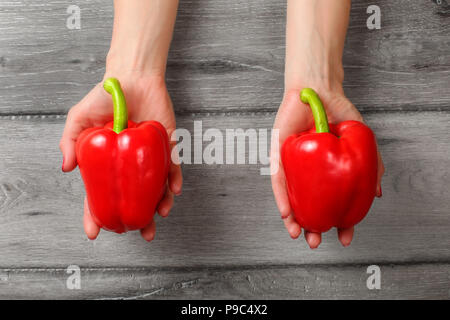 Draufsicht auf Frau Hände halten zwei rote Paprika über graues Holz Schreibtisch. Stockfoto