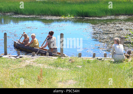 Ein Bügeleisen Alter Familie in einem hölzernen Canoe paddeling über dem Wasser auf das Land der Legenden in Lejre, Dänemark Stockfoto