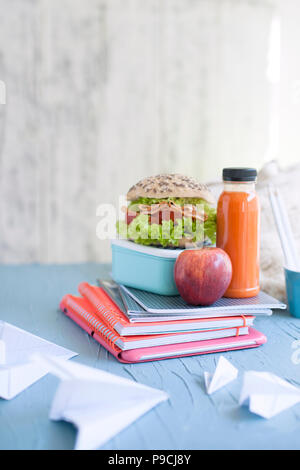 Schule Mittagessen in einer Box und Saft mit Obst auf einem grünen Hintergrund und Bücher auf einem Tisch. Toast und Saft in der Flasche. Freier Platz für Text. Platz kopieren Stockfoto
