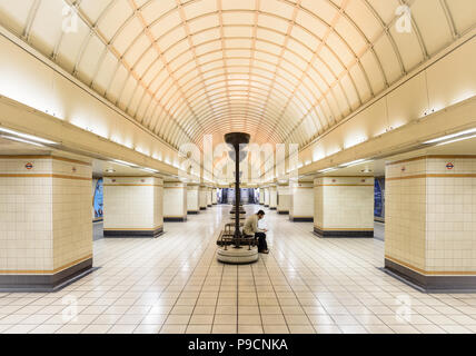 Mann allein am U-Bahnhof Gants Hill in London auf der Suche nach Handy während der Wartezeit auf die nächste U-Bahn Stockfoto