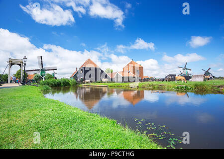 Windmühle und Blick auf den berühmten Platz von touristischen Zaanse Schans Farm und Industrie in Amsterdam, Niederlande, mit klaren, blauen Himmel und Reflexion auf dem Wasser Stockfoto