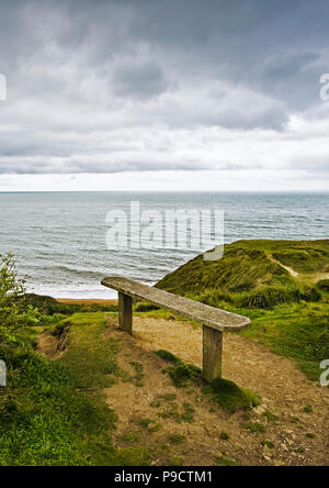 Alte Holzbank mit Blick auf das Meer von einer Klippe auf einem grauen bewölkten Tag, England, Großbritannien Stockfoto