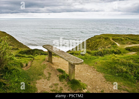 Alte Holzbank mit Blick auf das Meer von einer Klippe auf einem grauen bewölkten Tag, England, Großbritannien Stockfoto