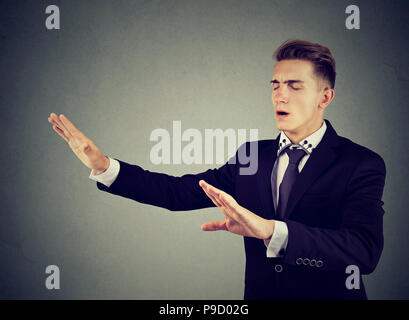 Junge Augen Mann im eleganten Anzug outstretching Hände und Suchen in der Dunkelheit auf grauem Hintergrund Stockfoto