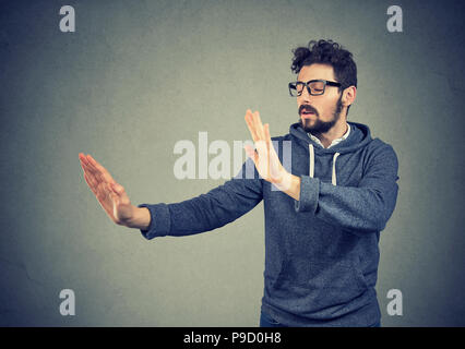 Junger Mann mit verbundenen Augen outstretching Hände und Suchen in der Dunkelheit auf grauem Hintergrund Stockfoto