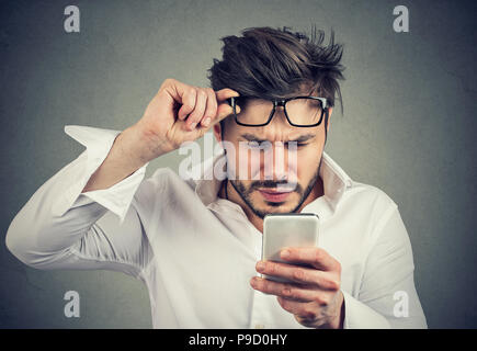 Junge formale Mann lesen Smartphone und Probleme mit den Augen blinzeln auf grauem Hintergrund Stockfoto