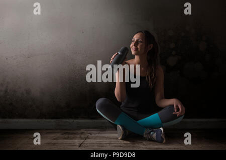 Läuferin Trinkwasser auf dem Boden sitzen, die Beine gekreuzt Stockfoto