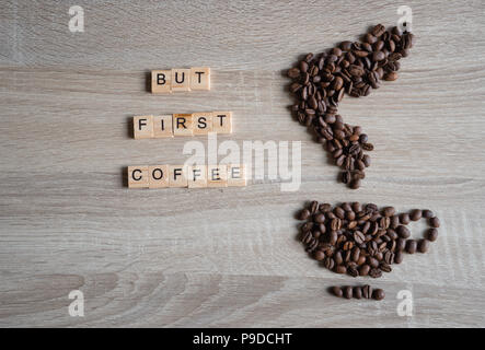 Geröstete Kaffeebohnen in der Form einer Tasse und Untertasse auf hölzernen Hintergrund platziert, mit Aber erste Kaffee Wort Stockfoto