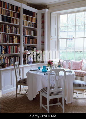 Bemalte Stühle mit geprüft Sitzen am Tisch mit einem weißen Tuch für das Mittagessen im Speisesaal ausgestattet mit Bücherregal eingestellt Stockfoto
