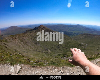 Ein mans hand greift über die Aussicht vom Gipfel des Mount Snowdon, Wales, UK. Mount Snowdon steht auf 1085 Meter über dem Meeresspiegel. Stockfoto