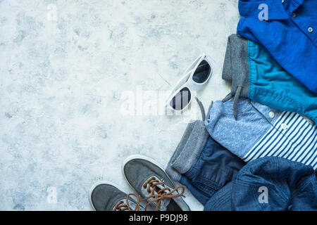 Kind Kleidung - Jeans, Polo, Shorts und Turnschuhen Draufsicht auf Stein Hintergrund. Mode Beauty Hintergrund. Modernes Aussehen. Flach kopieren. Stockfoto