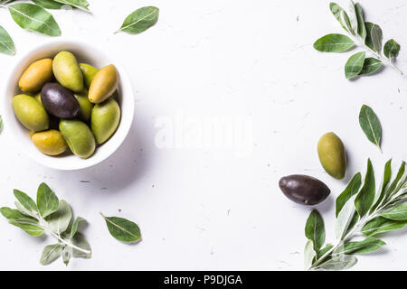 Schwarze und Grüne Oliven in eine Schüssel geben und Olivenblätter auf weißem Marmortisch. Ansicht von oben mit der Kopie. Stockfoto