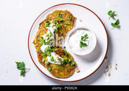 Zucchini Pfannkuchen mit grünen und saure Sahne auf weißer Tisch. Diät essen, fleischlose Gerichte. Stockfoto