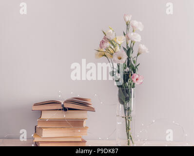 Eustoma blumen blumenstrauss in der Vase, der Alten vintage Bücher und girlande Lichter auf grauem Hintergrund. Lesen und Konzept entspannen Stockfoto