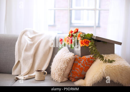 Tee Rosen in einer Geschenkbox, auf der Couch mit Kissen, in der Nähe der Fenster. Gemütlichkeit zu Hause. Guten Morgen. Freier Platz für Text oder eine Postkarte. Stockfoto