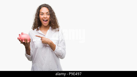 Junge Hispanic woman holding piggy Bank sehr zufrieden zeigte mit Hand und Finger Stockfoto