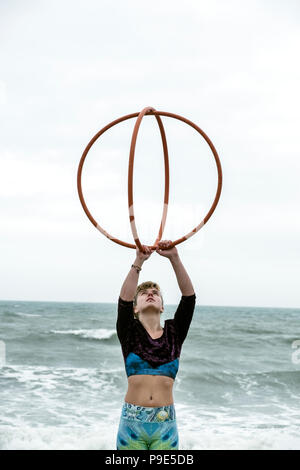 Junge Frau mit braunen Haaren und Dreadlocks stehen durch den Ozean, Balancing zwei Hula Hoops. Stockfoto