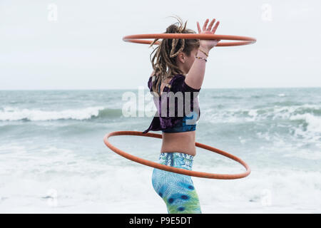 Junge Frau mit braunen Haaren und Dreadlocks stehen durch den Ozean, Balancing zwei Hula Hoops. Stockfoto