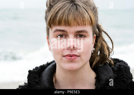 Porträt der jungen Frau mit braunem Haar und dreadlocks und eine Lippe Piercing mit schwarzen Fell jacke, an der Kamera schaut. Stockfoto