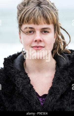 Porträt der jungen Frau mit braunem Haar und dreadlocks und eine Lippe Piercing mit schwarzen Fell jacke, an der Kamera schaut. Stockfoto