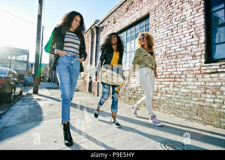 Drei junge Frauen mit Langen lockigen Haar entlang Pavement, einer trägt Skateboard. Stockfoto