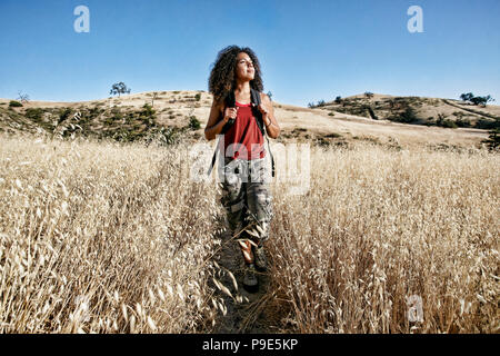 Junge Frau mit dem lockigen braunen Haar wandern in städtischen Park. Stockfoto