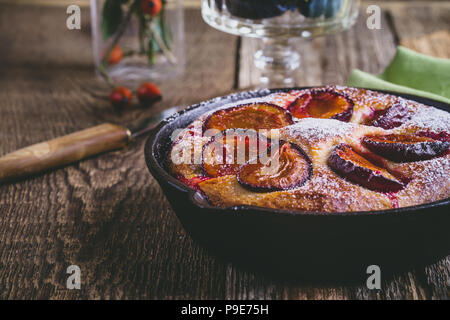 Hausgemachte Obst Torte mit frischen Pflaumen aus Gusseisen Skillet auf rustikalen Holztisch Stockfoto