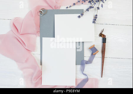 Weiße leere Karte mit zwei Trauringe auf einem Hintergrund von rosa Stoff mit Lavendelblüten und kalligraphischen Stift auf einem weißen Hintergrund. Mockup mit Umschlag und eine leere Karte. Flach. Ansicht von oben Stockfoto