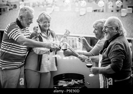 Ältere Erwachsene Gruppe in der Freizeit tun Grill BBQ auf der Dachterrasse zu Hause mit Bergblick. Essen und Wein für zwei Männer und zwei Stockfoto