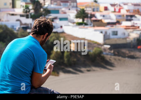 Mann von hinten mittels Mobiltelefon mit Internetzugang und app.Altstadt und Strand im Hintergrund. Sommer und Freizeit Entspannen Stockfoto