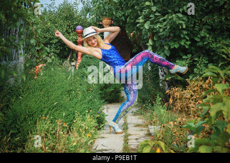 Junge lächelnde Mädchen in bunten Leggins, blau oben, weißen Hut und auf hohen Absätzen tanzen im Park Stockfoto