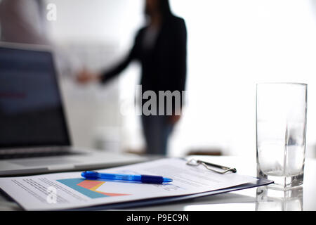 Laptop mit Ordner auf dem Schreibtisch, zwei Geschäftsleute stehen im Hintergrund Stockfoto