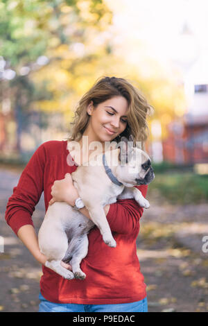 Hübsche Frau im Park mit ihren liebenswerten Französische Bulldogge Welpen. Herbst Zeit. Stockfoto