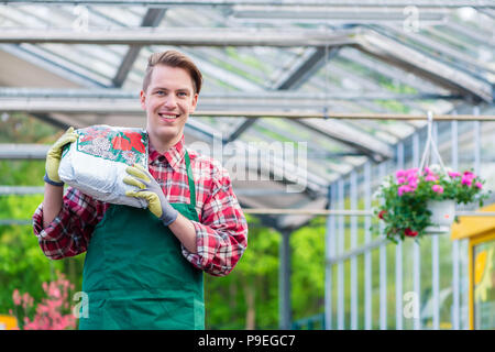 Fröhlicher junger Mann, der einen Sack Blumenerde während der Arbeit Stockfoto